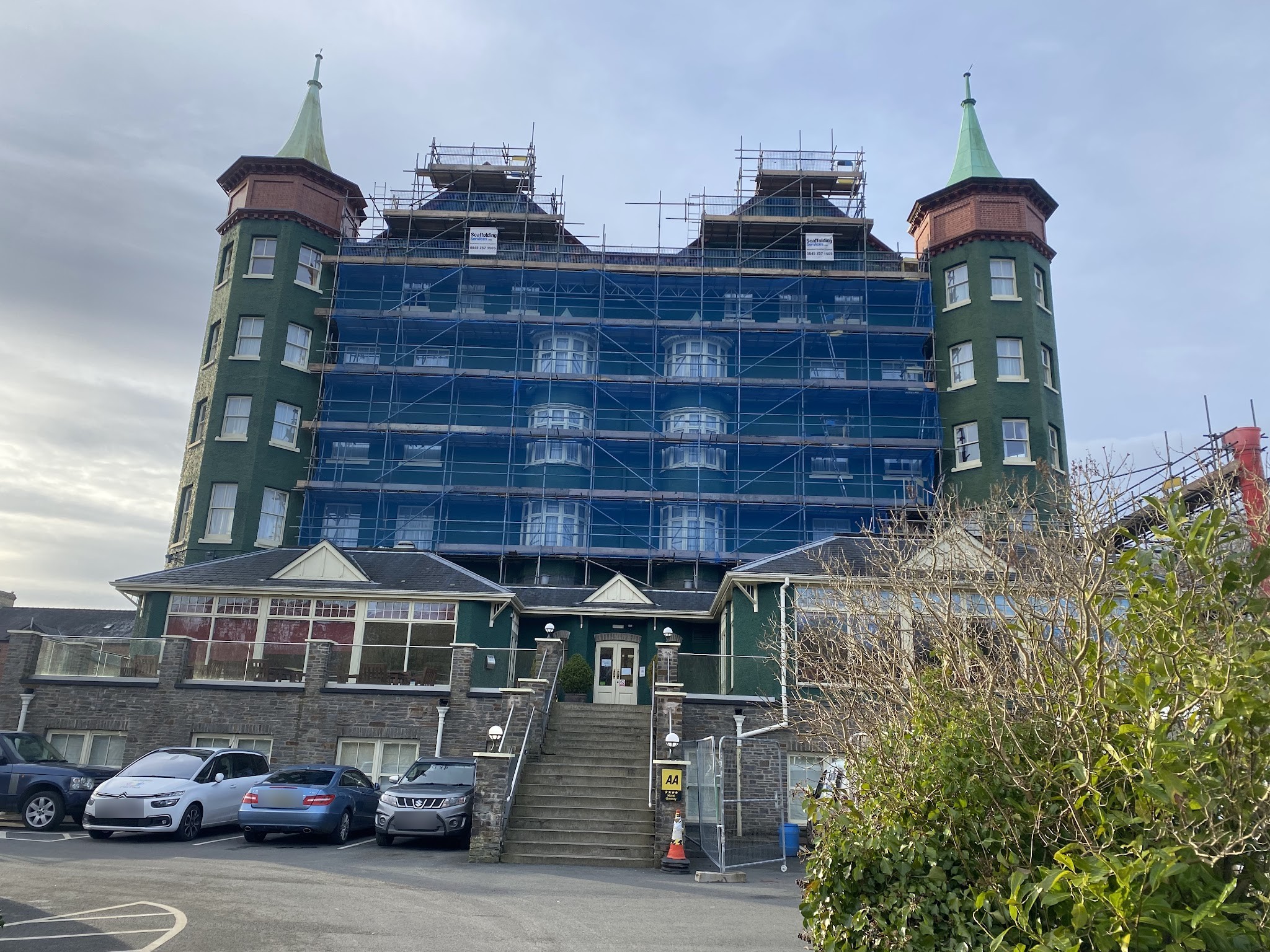 A tall Victorian hotel with green turrets fully scaffolded and netted