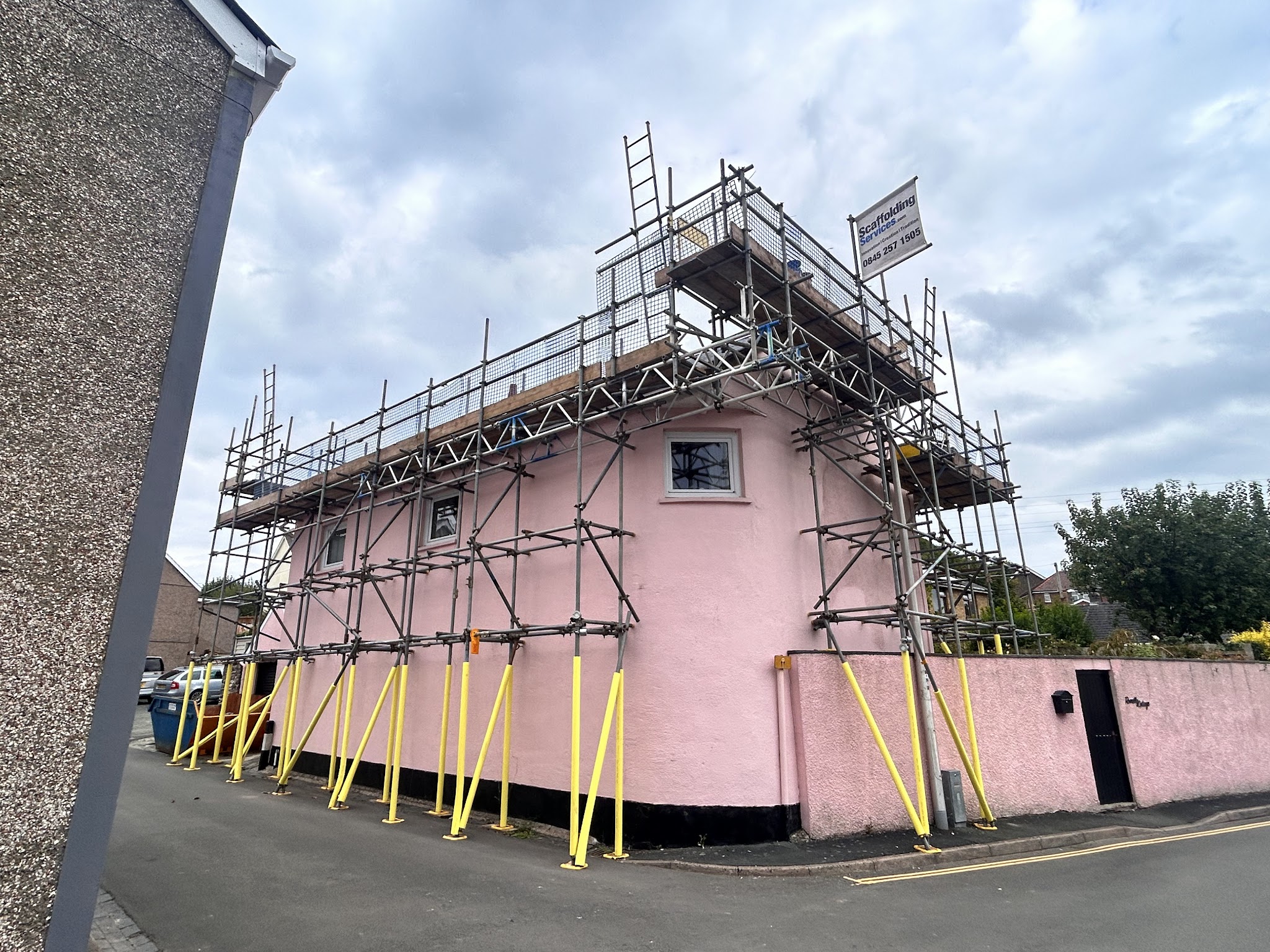 A pink rendered house scaffolded, with yellow raking shores along the base