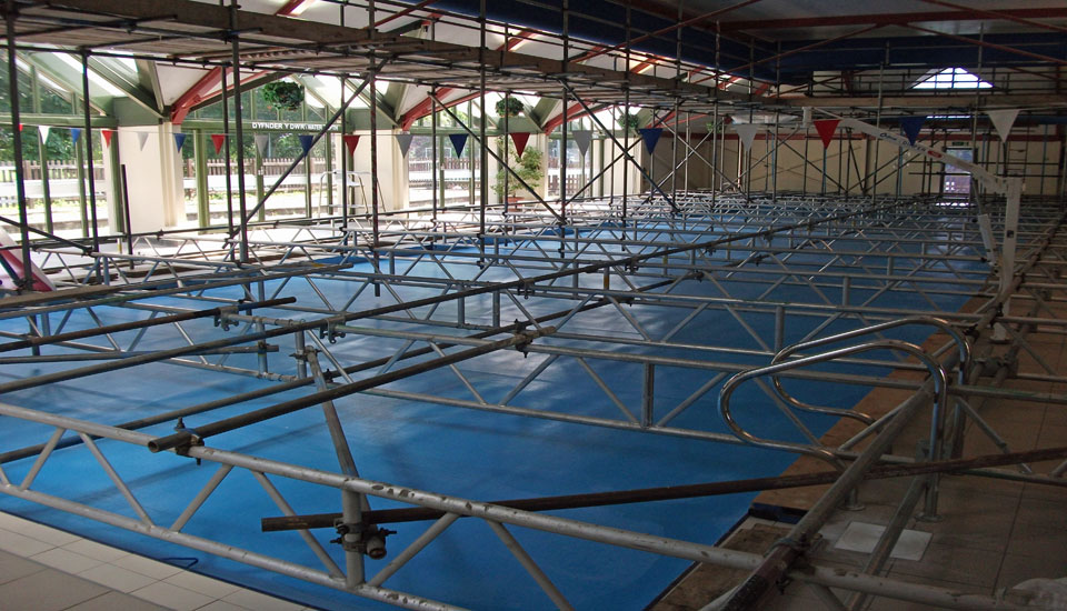 Scaffold beams spanning a covered swimming pool tank, bunting overhead