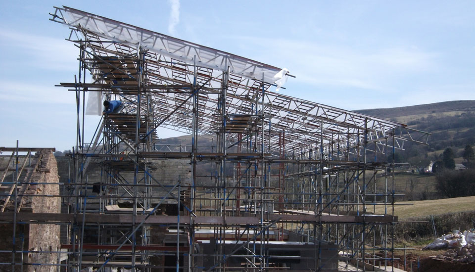A temporary roof frame of scaffold tube over a building on a hillside, hills behind